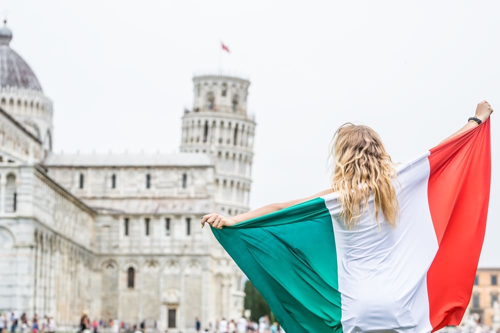 Mulher com a bandeira da Itália em frente à Torre de Pisa representando a importância da tradução juramentada em italiano para obter a cidadania.